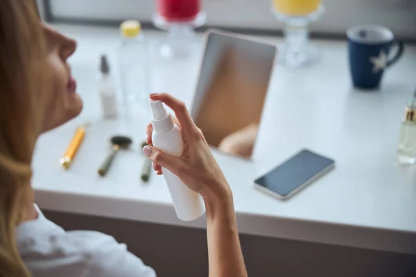 Jeune femme assise au bureau tout en prenant soin du visage le matin — Photo