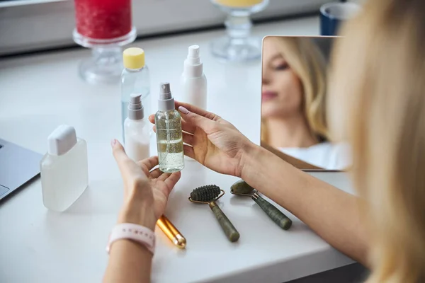 Mujer joven sosteniendo aceite orgánico esencial o suero sobre la mesa en el interior de la habitación —  Fotos de Stock