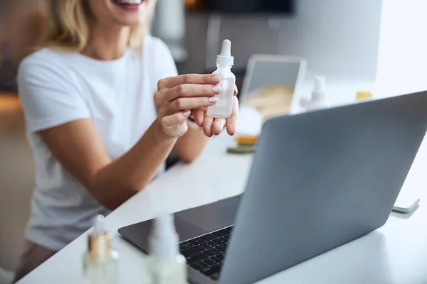 Business woman working at the laptop while demonstrating plastic bottle with serum on video call — Stock Photo, Image