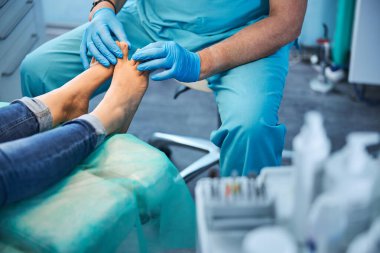 Doktor ayaklarına bakarken hasta tıbbi sandalyede oturuyor.