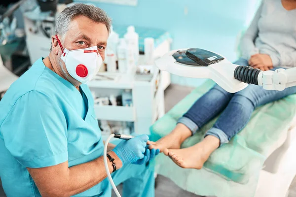 Professionell specialist kiropodist i blå handskar tittar på fotokameran i vårdcentralen — Stockfoto