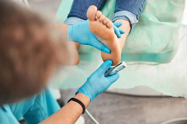 Pie derecho de la mujer en la mano quiropodista en el procedimiento de pedicura médica en la clínica de belleza —  Fotos de Stock