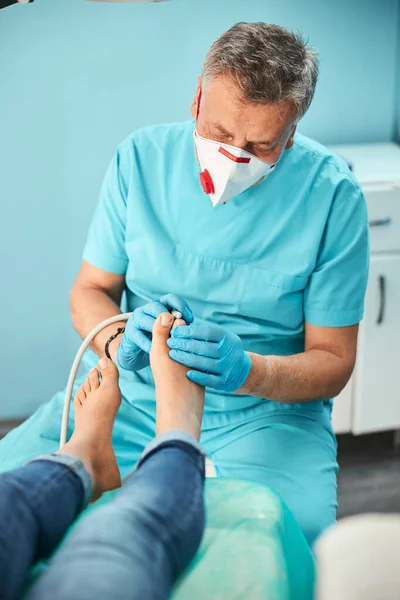 Unrecognized patient sitting in medical chair while doctor removing hard skin of foot