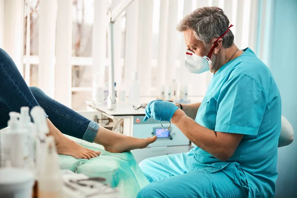 Bello adulto chiropodista utilizzando strumenti speciali durante il trattamento unghie incarnite — Foto Stock