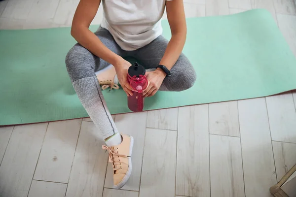 Senhora desportiva com uma bebida sentada no tapete de exercício — Fotografia de Stock