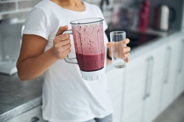 Mutfak tezgahına yaslanmış smoothie içen bir kadın.
