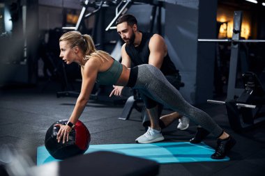 Spor salonunda topu kullanırken egzersiz yapan genç bir kadın.