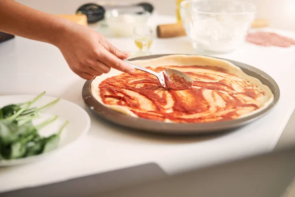 Cobrindo a base de pizza com molho de tomate — Fotografia de Stock