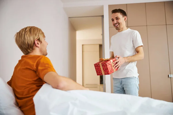Glada ung man ger present till sin pojkvän hemma — Stockfoto