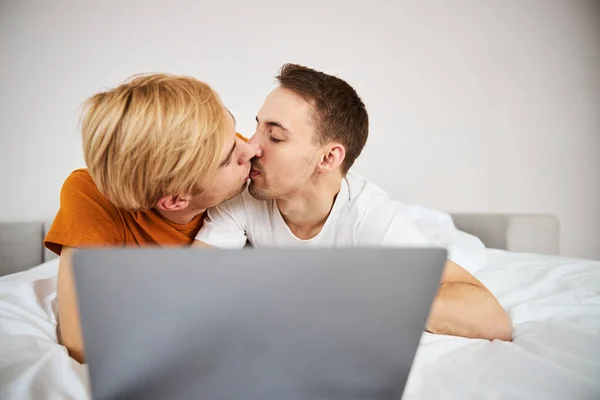 Liebendes homosexuelles Paar küsst und benutzt Laptop zu Hause — Stockfoto