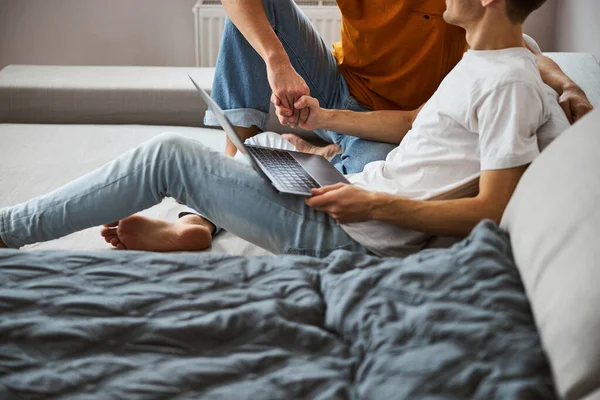 Feliz gay casal segurando mãos e usando laptop no casa — Fotografia de Stock