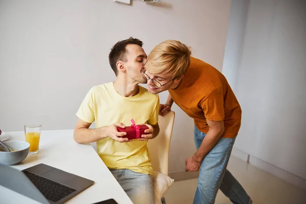 Schöner Mann hält Geschenk und küsst Freund zu Hause — Stockfoto