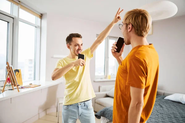 Glückliches homosexuelles Paar nutzt Smartphone und singt zu Hause — Stockfoto