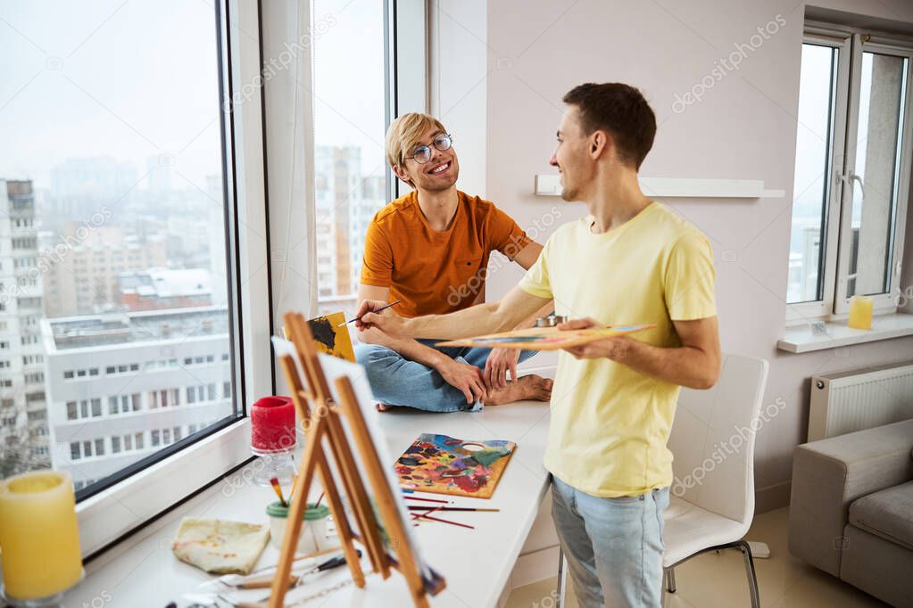 Cheerful man painting picture and chatting with boyfriend at home