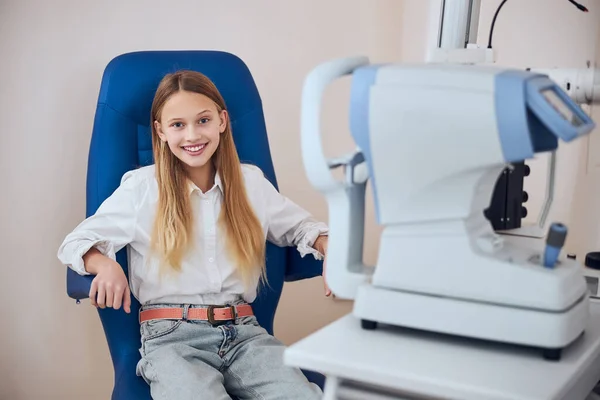 Jeune fille joyeuse en chemise blanche assise dans un fauteuil bleu à la clinique — Photo