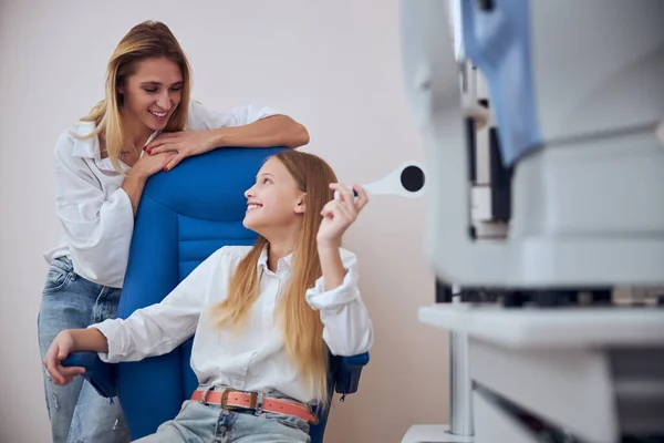 Glad glad glad blond kaukasiska mor talar med söt dotter i kontor pediatrisk ögonläkare — Stockfoto