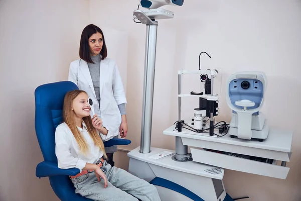 Sérieusement brunette médecin vérifier la vision de l'enfant et à la recherche de problèmes et de prendre soin des yeux — Photo