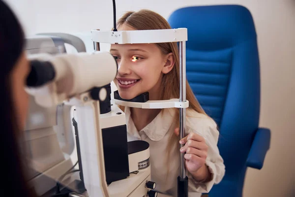 Hermosa chica adolescente hablando con el médico óptico mientras examinan su visión en el centro de oftalmología — Foto de Stock