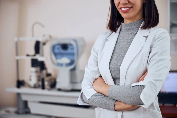 Okouzlující dospělá brunetka žena v bílé uniformě stojící v pokoji v interiéru na klinice — Stock fotografie