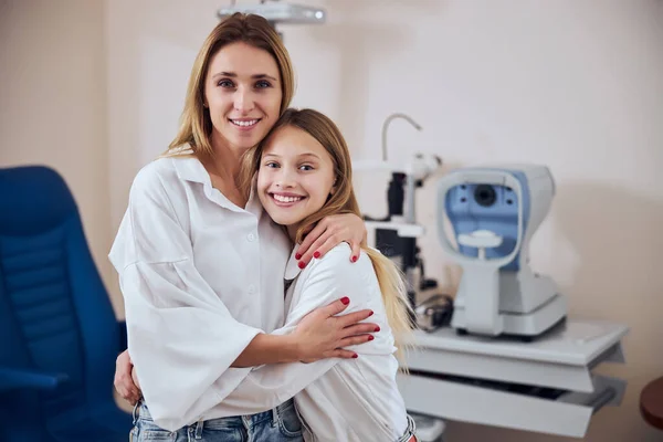 Szczęśliwa uśmiechnięta matka i córka pozowanie i patrząc w aparat fotograficzny w szafce optometrycznej — Zdjęcie stockowe