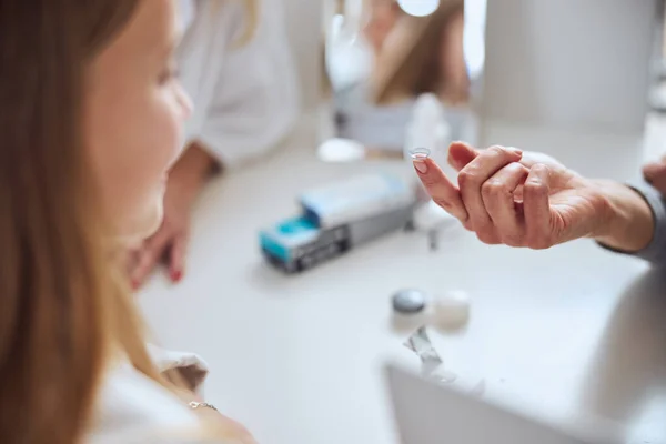 Imagen enfocada del brazo femenino por encima de la mesa mientras sostiene la lente en el dedo —  Fotos de Stock