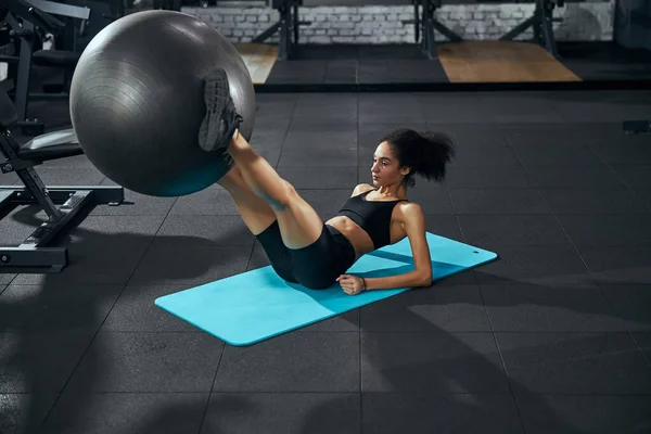 Yoğunlaşmış kadın bacaklı fitness topu kaldırıyor. — Stok fotoğraf