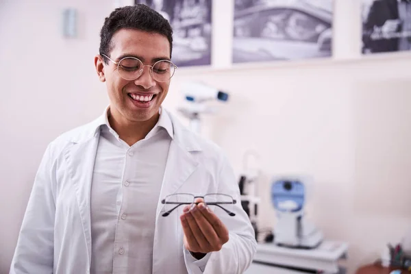 Optometrista sonriente mirando gafas graduadas en su mano — Foto de Stock