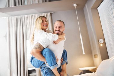 Neşeli adam gülümseyen karısını yatağa taşıyor.