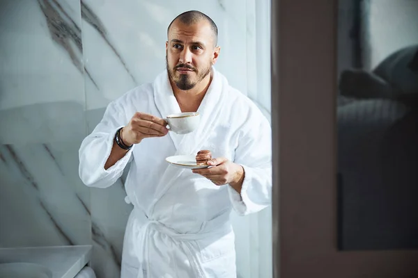 Homem pensativo com uma bebida e biscoitos no banheiro — Fotografia de Stock