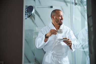 Elinde makaron ve elinde bir bardak tutan memnun bir adam.