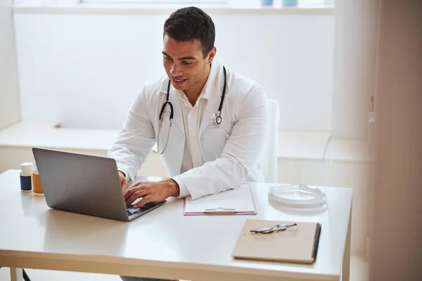 Médecin homme concentré assis au bureau avec des outils spéciaux à l'épaule dans la pièce à l'intérieur — Photo