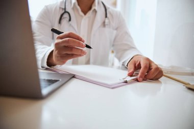 Terapist çalışma masasındaki belgelere steteskopla not yazıyor.