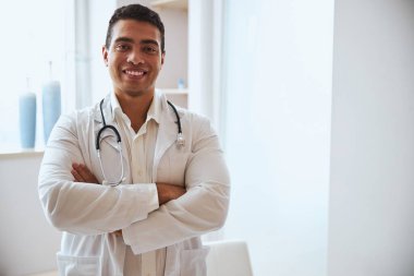 Steteskoplu mutlu Hintli genç stajyer tıp bürosundaki fotoğraf makinesine poz veriyor.