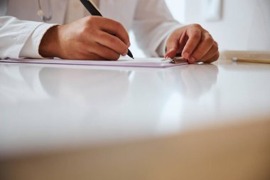 Doktorun masada otururken notlar alırken odaklanmış görüntüsü