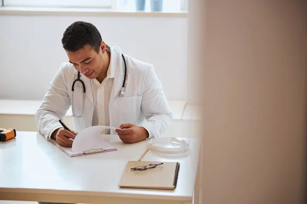 자신감 있는 의사가 내각 서류 작업을 하면서 책상에 앉아 있는 모습 — 스톡 사진