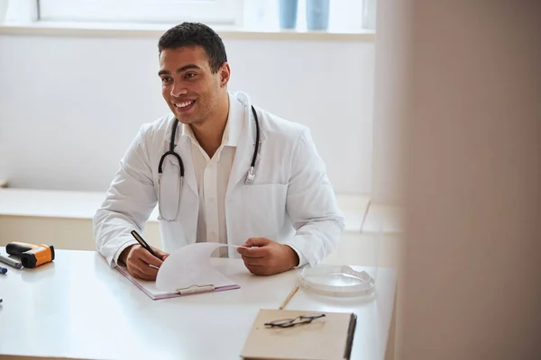 Joyeux médecin souriant assis au bureau dans la chambre à l'intérieur — Photo