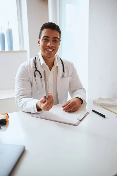 Médecin brune confiant avec stéthoscope assis au bureau du centre médical — Photo