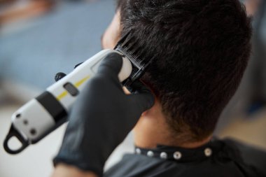 Koyu renk saçlı bir adam kuaförde vakit geçirirken yeni saç stili yaptırıyor.