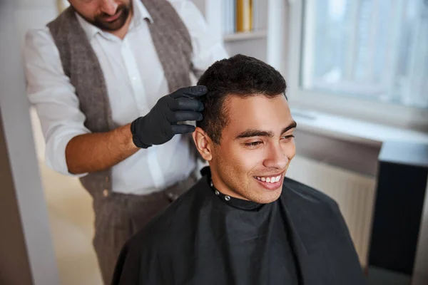 Man med glänsande starkt silkeslent hår sitter på stolen medan frisören gör frisyr i skönhetssalong — Stockfoto