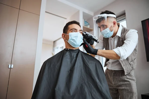 Два чоловіки в захисних масках роблять укладання волосся в кімнаті з сучасною машиною — стокове фото
