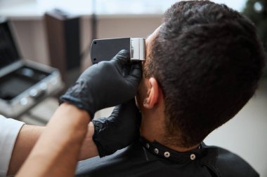 Tıp eldivenli berberlerin elleri modern makineleri tutuyor ve insan ziyaretçilerini küçümsüyor.