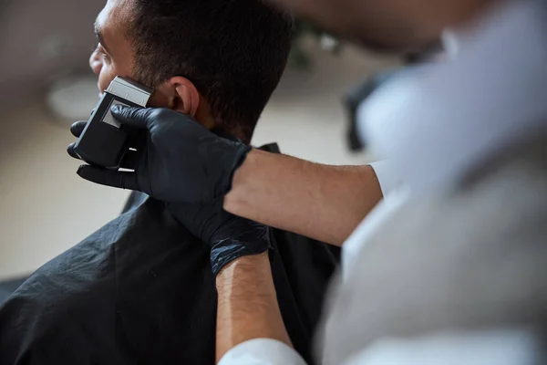 Bonito macho em preto peignoir descansando enquanto obtendo cabeleireiro na barbearia — Fotografia de Stock