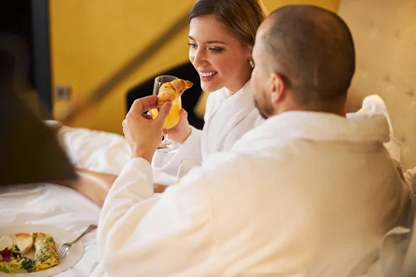 Hombre alimentando a una sonriente mujer complacida con un croissant — Foto de Stock