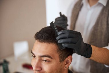 Güzellik salonundaki ziyaretçinin yanında elinde tarak tutan eldivenli berberin odaklanmış görüntüsü