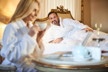 Sevinçli sakallı adam kız arkadaşına gülümsüyor ve kahve içiyor.