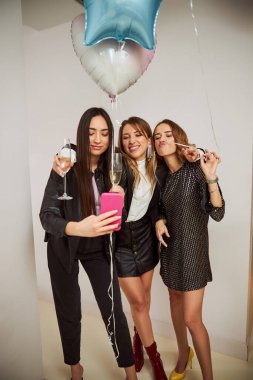 Şampanya kadehli üç kadın bir partide fotoğraf çekiliyor.