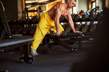 Spor salonunda bir çift dambıl kullanan ciddi bir vücut geliştirici.