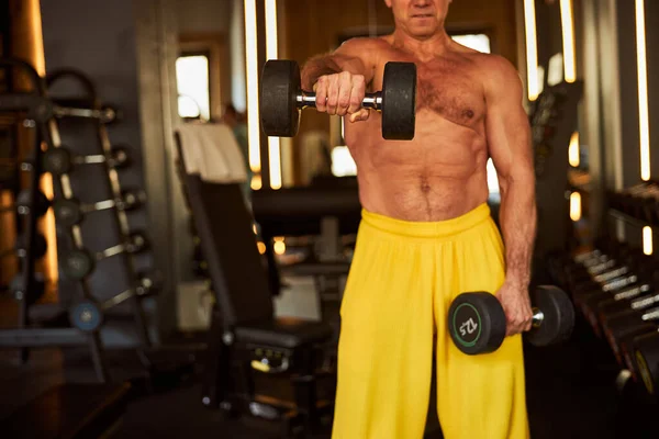 Focused sportsman lifting dumbbels and exercising at gym