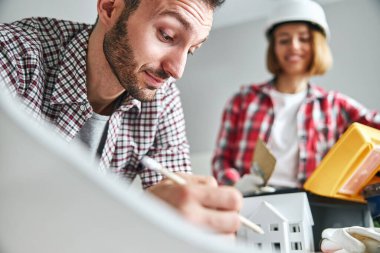 Neşeli kadın ressam, çalışan esmer sakallı bir ressama bakıyor.