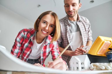 Neşeli çekici kadın bir ev planı çiziyor.